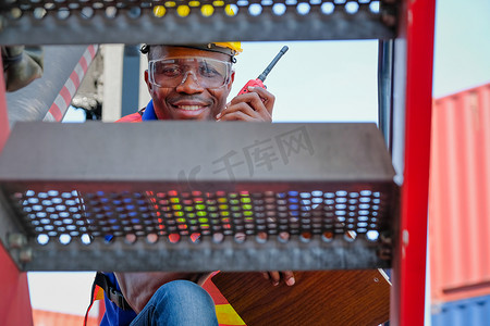 专业出口摄影照片_带对讲机的非洲技术人员通过货柜航运区大卡车的台阶进行观察。