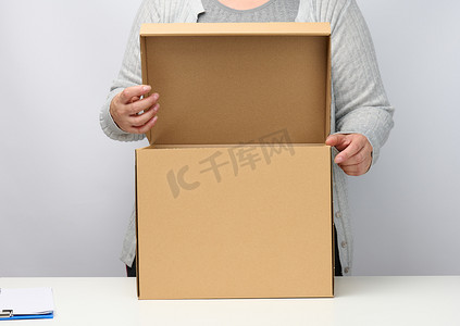 穿着灰色衣服的女人站着，拿着白色背景上打开的棕色盒子，移动、发送和交付货物