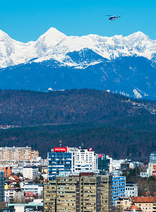 卢布尔雅那 — 2017 年 3 月，斯洛文尼亚：背景是雪山的卢布尔雅那市景和天空中飞翔的警用直升机