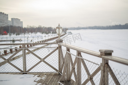 地球钟摄影照片_木制复古露天甲板上白雪，旧剥落油漆浅牛奶色，墙上挂着钢铜灯笼，下雪的冬天，雪躺在河上，地球的远岸是 vi