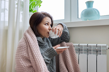 冬季，妇女在家庭暖气散热器附近取暖