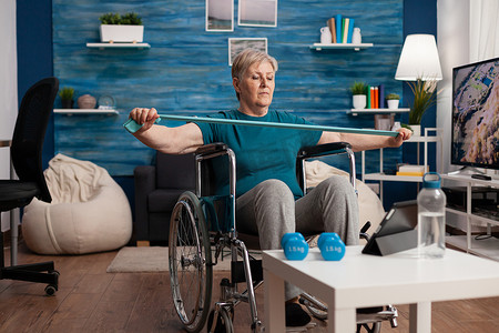 坐在轮椅上的残疾老妇人用松紧带拉伸手臂阻力训练身体肌肉