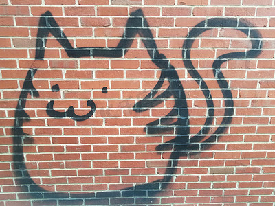 红砖墙上有尾巴的黑色涂鸦动物