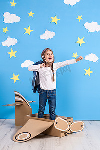 小梦想家女孩在蓝天白云背景的工作室里玩纸板飞机。