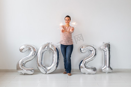 2021快乐摄影照片_新年庆祝活动和派对理念 — 快乐的年轻女人，在白色背景的 2021 年银色气球附近放着火花。