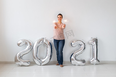 新年庆祝活动和派对理念 — 快乐的年轻女人，在白色背景的 2021 年银色气球附近放着火花。