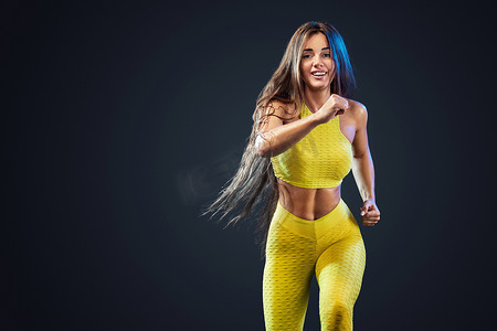 强壮的运动，女子短跑运动员，穿着黄色运动服，在黑色背景下跑步，健身和运动动机。