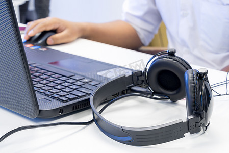 键盘耳机鼠标摄影照片_男子手使用键盘和鼠标来控制带 headpho 的笔记本电脑