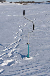 冰钻摄影照片_在冰上钻洞和雪中渔夫的痕迹