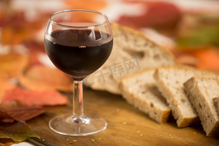 秋天的味道和颜色：一杯红酒，背景是一片全麦面包，放在一块旧木切板上，周围有红色和橙色的紫藤叶
