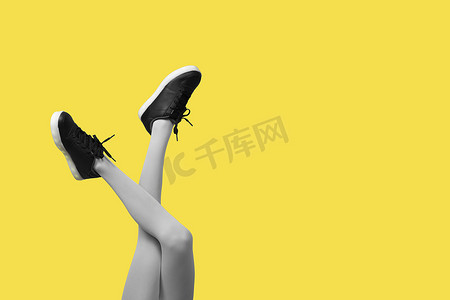 新的黑色女性运动鞋在细长的女性腿上，穿着灰色紧身裤，与黄色背景隔离。