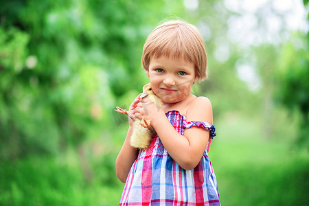 夏日太阳裙的小女孩拥抱一只站在草地上大自然的小鸭