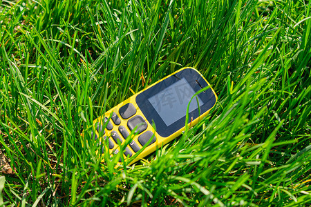 垃圾污染摄影照片_破碎的旧手机被扔进茂密的草丛中