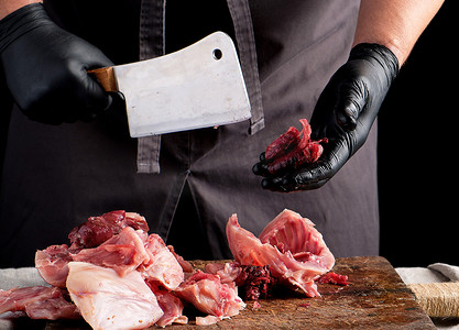 血淋淋的摄影照片_黑色乳胶块的厨师将生兔肉切成碎片