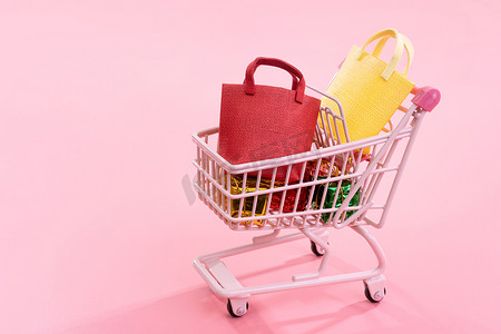 年度销售购物季概念 — 迷你红色购物车手推车，里面装满纸袋礼品，以淡粉色背景隔开，空白复制空间，特写