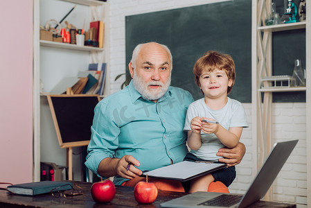 友好的小男孩和老成熟的老师在黑板桌附近的教室里。