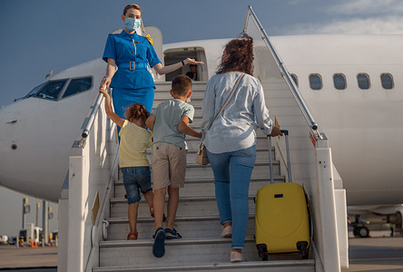 母亲带小孩摄影照片_母亲带着两个小孩和手提箱登机的背影。