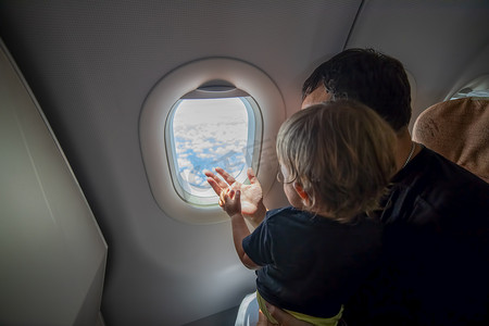 父亲和可爱的小孩坐在飞机上，透过舷窗看着天空。