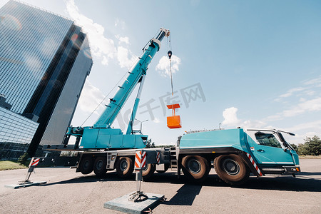 一台大型蓝色卡车起重机在一座大型现代建筑附近的工地上准备就绪。