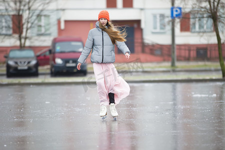 女孩少年在城市的冰上溜冰。穿着长裙和保暖夹克的年轻女孩在冰上。