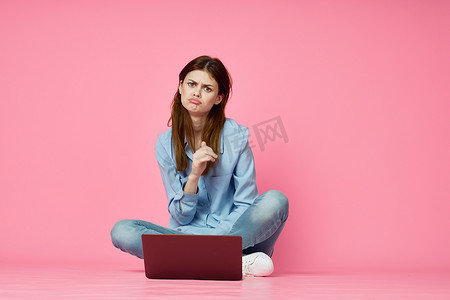 女人坐在地板上，笔记本电脑购物娱乐粉红色背景