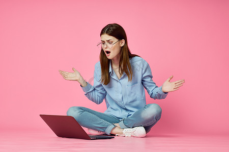 女人坐在地板上，笔记本电脑购物娱乐粉红色背景