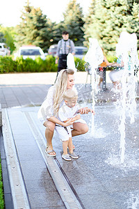 年轻快乐的母亲和小孩坐在喷泉附近。