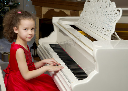 美丽的小女孩正在一架白色三角钢琴上弹奏。