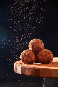 自制巧克力松露，在深色背景的木板上筛可可粉。