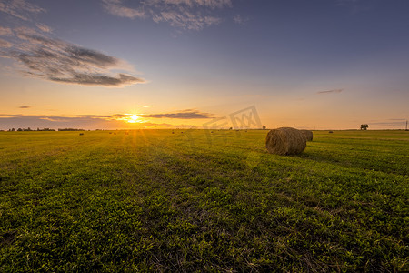 田野夕阳摄影照片_夏日傍晚夕阳下的干草堆田野。
