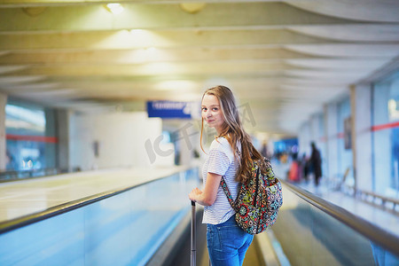 背着行李的人摄影照片_背着背包的旅游女孩，在国际机场带着行李，在自动人行道上