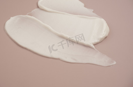 白色乳液摄影照片_粉红色背景上的白色美容霜乳液荧光笔涂抹色板污迹