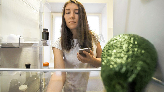 冰箱旁的女人用智能手机列出食物清单
