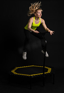 黑色背景健身蹦床上的女孩穿着黄色 T 恤蹦床健身运动，锻炼运动员健康的有氧运动，锻炼飞行中心运动，身体肌肉教练享受