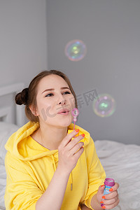 肥皂泡泡摄影照片_黄色迷人的年轻女子的画像，在明亮的灰色背景上的肥皂泡泡中。
