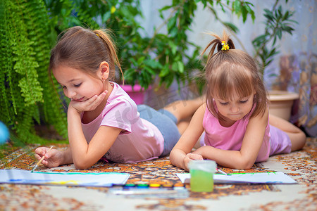 两个女孩在家里或幼儿园的地板上用颜料作画。