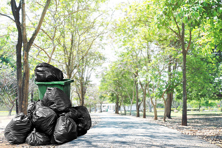 污染塑料袋摄影照片_步行道旁的垃圾桶绿色回收和垃圾塑料袋，公园自然背景下街道底层的许多垃圾塑料袋，用于环境清洁概念、污染废物