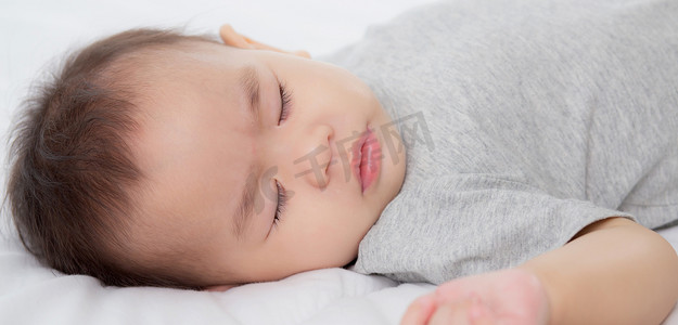 睡前床摄影照片_睡在家里卧室床上的亚洲小女婴的肖像，新生儿在舒适和放松的情况下打盹，睡前的婴儿纯真，快乐的幼儿可爱，孩子的成长和情感，在室内。