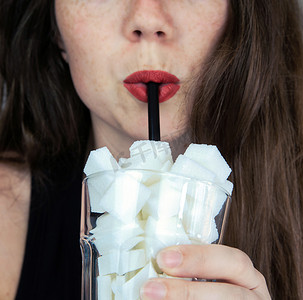 年轻女子用装满方糖的玻璃杯中的黑色吸管喝酒的肖像垃圾食品、不健康饮食、饮料中糖分过多、营养概念