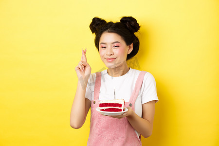 化着迷人妆容的生日快乐女孩，许愿庆祝，交叉手指梦想成真，黄色背景中拿着蛋糕站着