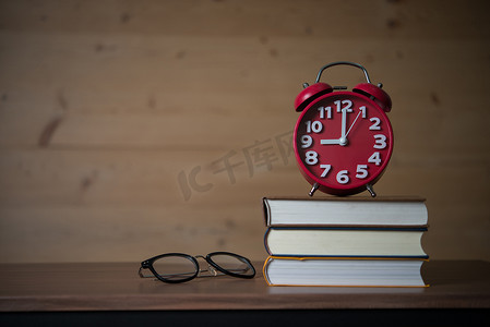 9点摄影照片_早上 9 点的闹钟，在木桌上戴着眼镜的一摞书上