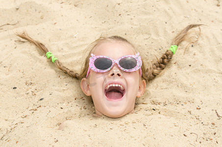海滩上戴眼镜的五岁女孩头枕在沙子里