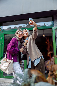 女人吐舌头摄影照片_与亚洲朋友嬉戏的成熟女性在现代城市街道上自拍吐舌头