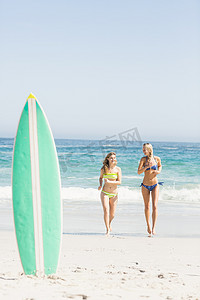 沙滩上的冲浪板和两个女人在海滩上跑步