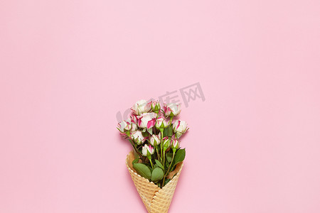 粉色背景贺卡摄影照片_粉色背景华夫饼锥中的小玫瑰，复制空间。