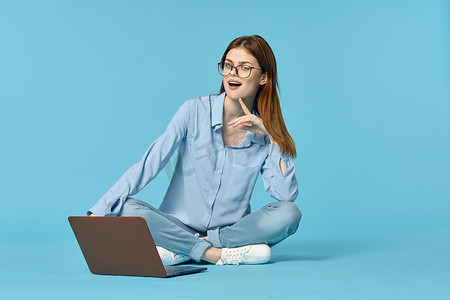 带笔记本电脑的女人坐在地板上学习学生技术蓝色背景