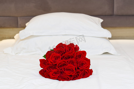 在酒店房间度蜜月的床上放着一束红玫瑰。