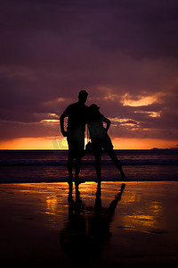 情侣牵手的剪影，日落时分快乐的年轻情侣在海滩上相爱