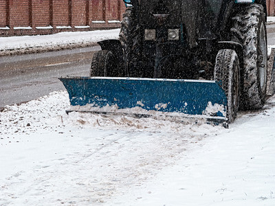 拖拉机用除雪机和旋转刷清除人行道上的积雪。