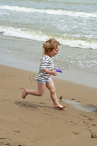 一个小男孩沿着海边的沙滩跑